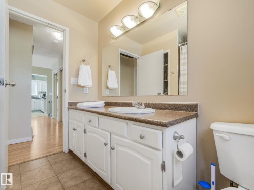 Vanity featuring white cabinetry with brushed nickel hardware, a speckled countertop, and an integrated sink with a chrome faucet - 2035 49A Street, Edmonton, AB 