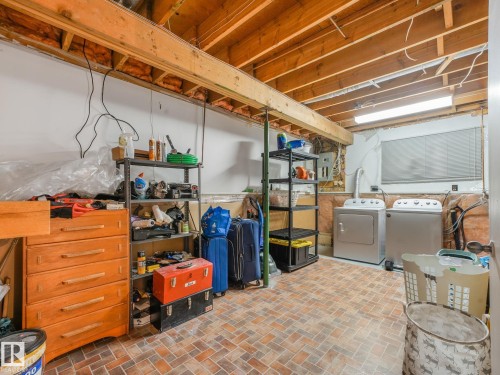 Laundry area featuring a side-by-side washer and dryer, brick-patterned floor tiles, exposed wood ceiling joists, and a window with horizontal blinds - 2035 49A Street, Edmonton, AB 