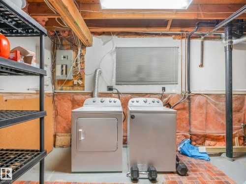Dedicated laundry area featuring a white washing machine and dryer, exposed ceiling joists, and brick-patterned flooring - 2035 49A Street, Edmonton, AB 