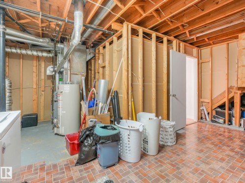 Unfinished basement with exposed wood framing, brick-patterned flooring, and a white interior door - 2035 49A Street, Edmonton, AB 