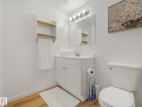 Bathroom featuring a white vanity with integrated sink, chrome faucet, wall-mounted mirror with vanity lighting, and wood-finish flooring - 2035 49A Street, Edmonton, AB 