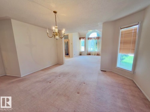 Spacious interior featuring a brass chandelier, multiple windows, arched window, and neutral wall tones - 134 Wolf Ridge Place, Edmonton, AB 