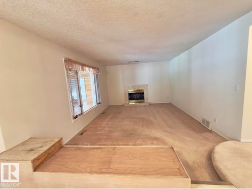 Spacious interior featuring a bay window, an ornate fireplace with a brass firebox, and a built-in multi-level platform - 134 Wolf Ridge Place, Edmonton, AB 