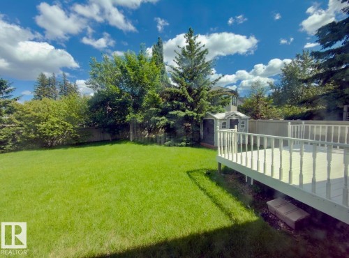 Expansive green lawn featuring a wooden privacy fence, mature trees, a detached storage shed, and a painted wood deck with balusters - 134 Wolf Ridge Place, Edmonton, AB 
