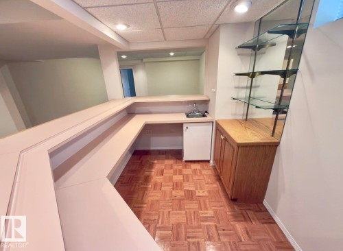 Wet bar featuring a compact refrigerator, stainless steel sink, wood-finish base cabinetry, and mirrored wall with glass shelving - 134 Wolf Ridge Place, Edmonton, AB 