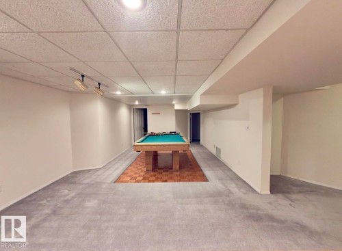 Expansive recreation room featuring a drop ceiling with recessed lighting and track lighting, grey carpeting, and a wood-finish flooring section - 134 Wolf Ridge Place, Edmonton, AB 