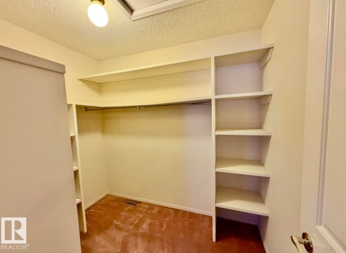 Walk-in closet featuring built-in shelving, hanging rod, textured ceiling, and flush-mount lighting - 134 Wolf Ridge Place, Edmonton, AB 