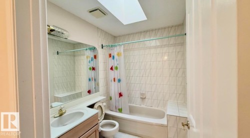 Bathroom featuring a white bathtub, ceramic tile shower surround, single vanity, and skylight - 134 Wolf Ridge Place, Edmonton, AB 