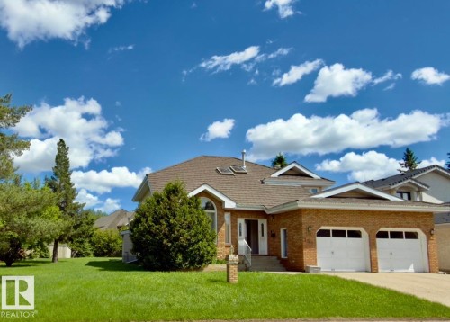 Brick exterior featuring a two-car garage with white doors, a front entrance with a white railing, a pitched shingle roof, and a manicured front lawn - 134 Wolf Ridge Place, Edmonton, AB 