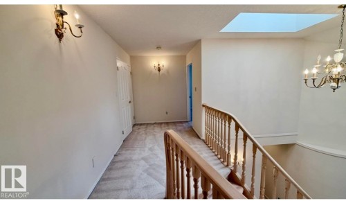 Carpeted hallway with a central skylight, wood-finish stair railing, and multiple wall sconces providing ambient lighting - 134 Wolf Ridge Place, Edmonton, AB 
