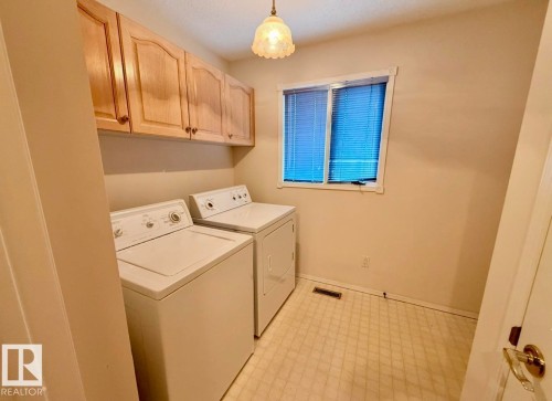 Dedicated laundry area with upper wood cabinetry, a window with blinds, and patterned vinyl flooring - 134 Wolf Ridge Place, Edmonton, AB 