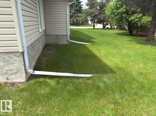 Exterior siding in a neutral tone with white downspouts, featuring a textured foundation and a verdant lawn - 134 Wolf Ridge Place, Edmonton, AB 
