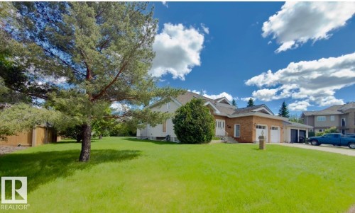 Brick and siding exterior featuring a two-car garage, multiple roof gables, a mature front yard tree, and an expansive lawn - 134 Wolf Ridge Place, Edmonton, AB 