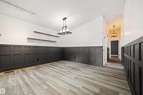 Spacious interior featuring contemporary wainscoting, wood-finish flooring, a modern chandelier, track lighting, and floating wood shelves - 28 Goodridge Drive, St. Albert, AB 