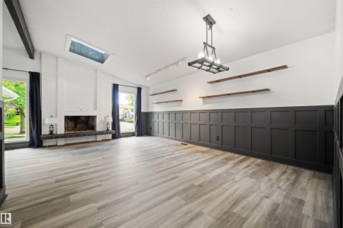 Spacious living area featuring a white brick fireplace with a dark hearth, vaulted ceiling with exposed beams, and a skylight - 28 Goodridge Drive, St. Albert, AB 