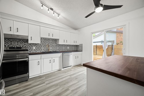 Kitchen featuring white cabinetry, patterned tile backsplash, wood-finish countertops, stainless steel appliances, and light wood-finish flooring - 28 Goodridge Drive, St. Albert, AB 