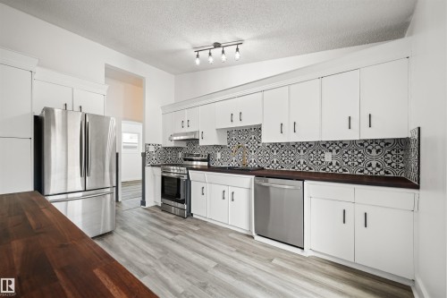 Bright kitchen featuring wood-finish flooring, white cabinetry with black hardware, dark wood-finish countertops, and a patterned tile backsplash - 28 Goodridge Drive, St. Albert, AB 
