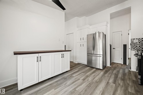 Kitchen area featuring wood-finish flooring, white cabinetry with dark hardware, a stainless steel refrigerator, and a dark wood-finish countertop - 28 Goodridge Drive, St. Albert, AB 
