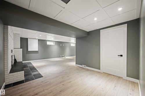 Spacious lower level featuring wood-finish flooring, recessed lighting, and a white brick fireplace with a dark tile hearth - 28 Goodridge Drive, St. Albert, AB 