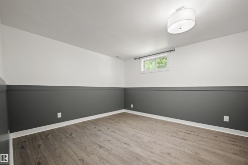 Room featuring wood-finish flooring, white baseboards, and two-tone walls with a dark gray lower section and white upper section - 28 Goodridge Drive, St. Albert, AB 