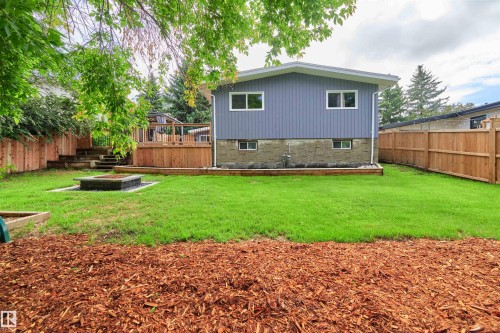 Backyard featuring a wooden deck with railing, a built-in fire pit, manicured lawn, and natural wood fencing - 28 Goodridge Drive, St. Albert, AB 