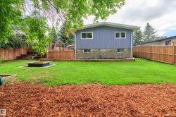 Backyard featuring a wooden deck with railing, a built-in fire pit, manicured lawn, and natural wood fencing - 