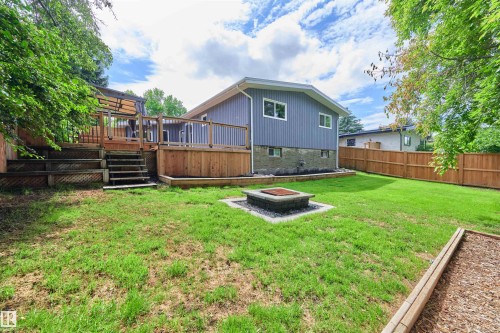 Expansive backyard featuring a multi-level wood deck, a built-in fire pit with stone surround, a wood fence, and a dedicated garden bed - 28 Goodridge Drive, St. Albert, AB 