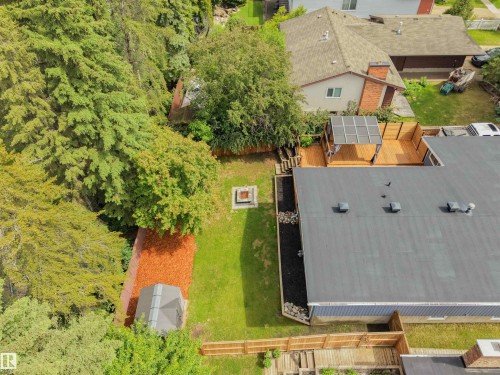 Expansive backyard featuring a large wooden deck with a covered pergola, a flat-roofed structure, a manicured lawn, a fire pit, and mature trees providing natural screening - 28 Goodridge Drive, St. Albert, AB 