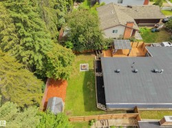Expansive backyard featuring a large wooden deck with a covered pergola, a flat-roofed structure, a manicured lawn, a fire pit, and mature trees providing natural screening - 