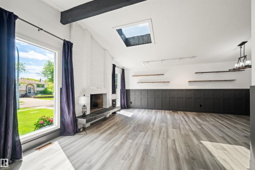 Spacious room featuring light wood-finish flooring and a white brick fireplace with a dark tile hearth - 28 Goodridge Drive, St. Albert, AB 