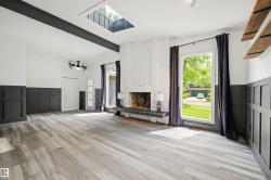 Spacious room featuring wood-finish flooring, a brick fireplace with a tile hearth, and a skylight - 