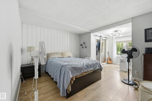 Bedroom featuring wood-finish flooring, a decorative accent wall, built-in shelving, and a bright window - 12326 92 Street, Edmonton, AB - Indoor Photo Showing Bedroom