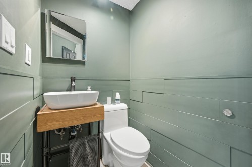 Modern powder room featuring a white vessel sink, wood-finish vanity, and a matte black faucet - 12326 92 Street, Edmonton, AB - Indoor Photo Showing Bathroom