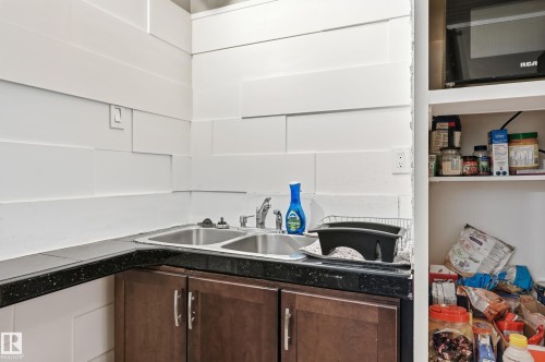 Compact kitchen area featuring a double-basin stainless steel sink, dark speckled countertop, and wood-finish lower cabinetry - 12326 92 Street, Edmonton, AB - Indoor Photo Showing Kitchen With Double Sink