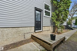Exterior side entrance featuring a wooden deck, vinyl siding, stucco foundation, and a mature tree - 