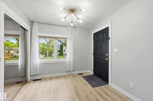 Entry area featuring a dark paneled door with brass hardware, wood-finish flooring, and a modern sputnik-style ceiling light - 12326 92 Street, Edmonton, AB - Indoor Photo Showing Other Room