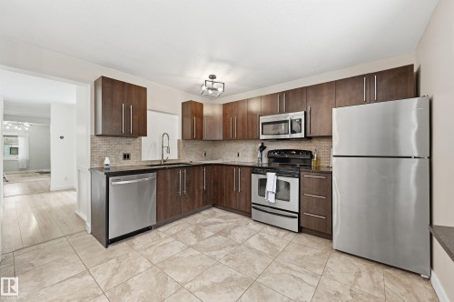 Kitchen featuring stone-look tile flooring, dark wood-finish cabinetry, stainless steel appliances, and a tiled backsplash - 12326 92 Street, Edmonton, AB - Indoor Photo Showing Kitchen