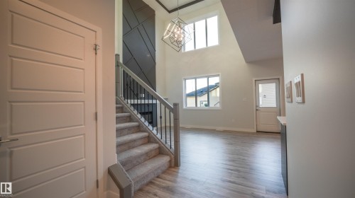 Two-story foyer with high ceilings, featuring a modern chandelier and a striking dark accent wall with geometric paneling - 44 Dalquist Bay, Leduc, AB 