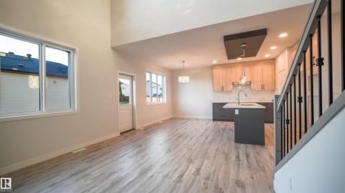 Open-concept living space featuring wood-finish flooring, a contemporary kitchen, a kitchen island with sink, and a staircase with metal balusters - 44 Dalquist Bay, Leduc, AB 