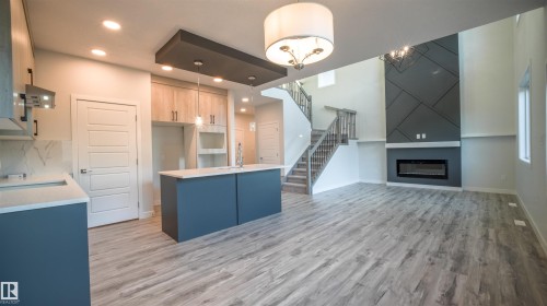 Open-concept living area featuring light wood-finish flooring, a contemporary kitchen island with a white countertop, and a statement fireplace with geometric detailing - 44 Dalquist Bay, Leduc, AB 