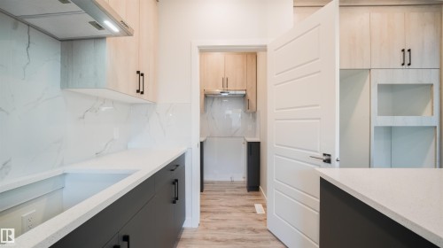 Modern kitchen featuring light wood-finish upper cabinetry and dark lower cabinetry with black hardware - 44 Dalquist Bay, Leduc, AB 