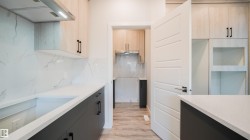 Modern kitchen featuring light wood-finish upper cabinetry and dark lower cabinetry with black hardware - 