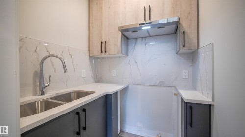 Compact kitchen featuring a dual basin stainless steel sink with a high-arch faucet, light wood-finish upper cabinetry, and dark lower cabinetry - 44 Dalquist Bay, Leduc, AB 