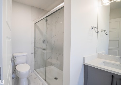 Modern bathroom featuring a glass-enclosed shower with tile surround, a white toilet, and a vanity with a light-colored countertop and a built-in sink - 44 Dalquist Bay, Leduc, AB 