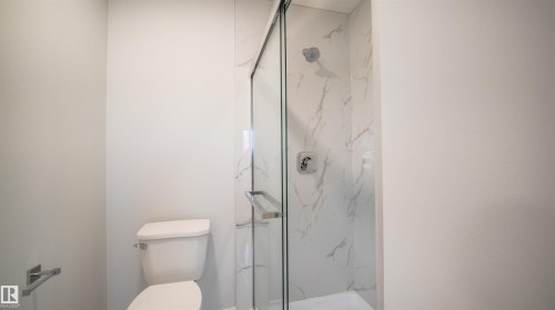 Glass-enclosed shower with white marble-look tile surround and chrome fixtures - 44 Dalquist Bay, Leduc, AB 
