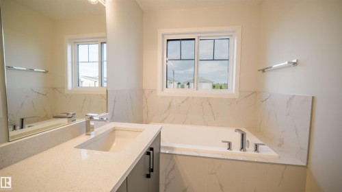 Bathroom featuring an undermount sink, quartz countertop, chrome fixtures, built-in bathtub, and marble-look wall tiling - 44 Dalquist Bay, Leduc, AB 