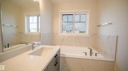 Bathroom featuring an undermount sink, quartz countertop, chrome fixtures, built-in bathtub, and marble-look wall tiling - 