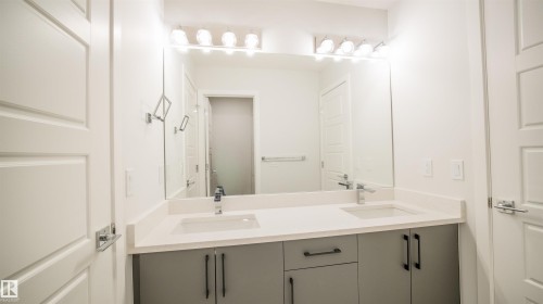 Modern double vanity featuring a light-toned countertop, dual integrated sinks, and contemporary gray cabinetry with black hardware - 44 Dalquist Bay, Leduc, AB 