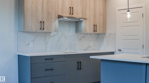 Modern kitchen featuring two-tone cabinetry with light wood-finish upper cabinets and matte gray base cabinets - 44 Dalquist Bay, Leduc, AB 