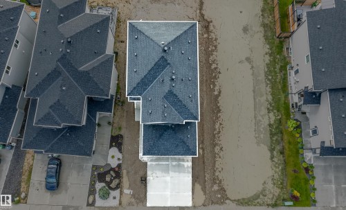 Newly constructed residence featuring a multi-gabled roofline with dark shingles, a concrete driveway, and an undeveloped lot - 44 Dalquist Bay, Leduc, AB 